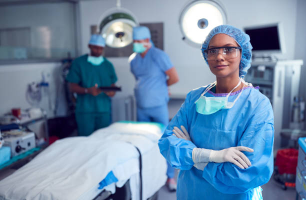 Portrait Of Female Surgeon Wearing Scrubs And Protective Glasses In Hospital Operating Theater Portrait Of Female Surgeon Wearing Scrubs And Protective Glasses In Hospital Operating Theater anaesthetist stock pictures, royalty-free photos & images