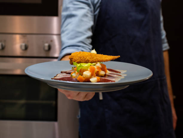 istock chef holding a culinary appetizer on a plate in kitchen. duck white vegatables 1204002732