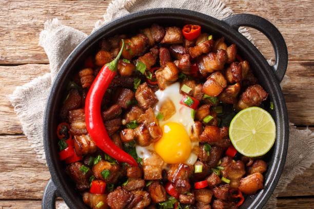 istock Sizzling spicy pork sisig with egg ang lime close-up in a pan. Horizontal top view 1204003454