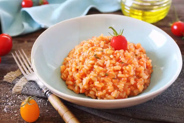 Italian cuisine. Plate of tomato risotto, olive oil and cherry tomatoes on wooden background