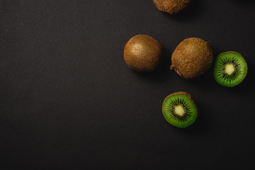 Kiwi fruits half sliced on dark black moody plain background, copy space, top view