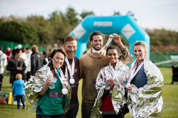 Friends smiling with medals after charity run Happy group of friends wrapped in foil blankets after Stampede race, fundraising, achievement, togetherness stampeding photos stock pictures, royalty-free photos & images