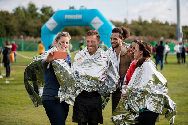 Cheerful runners in foil blankets taking selfie Mixed race group photographing themselves after finishing race at Stampede event, achievement, success, togetherness stampeding photos stock pictures, royalty-free photos & images