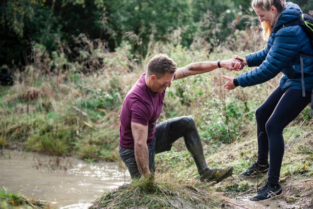 Woman helping man out of muddy stream Woman pulling friend out of stream onto muddy bank, determination, a helping hand, outdoors stampeding photos stock pictures, royalty-free photos & images