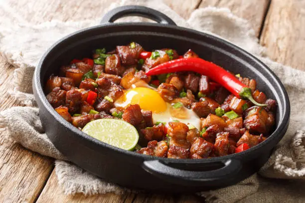 Photo of Sizzling spicy pork sisig with egg ang lime close-up in a pan. Horizontal