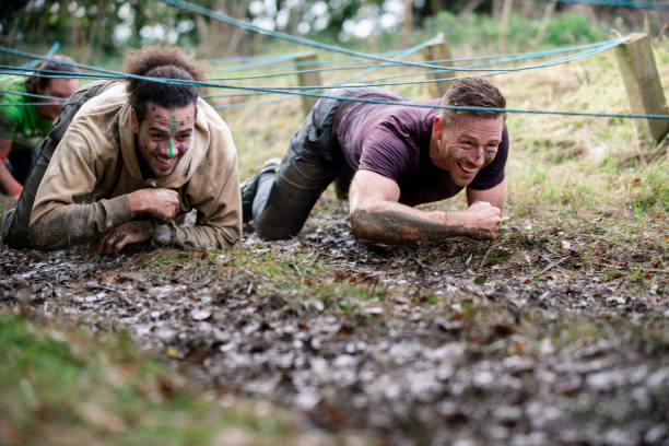 Cheerful muddy men clambering through mud together in cross country event, determination, male friendship, fitness