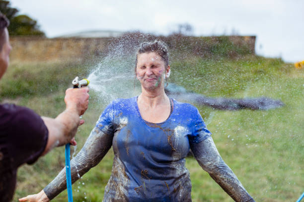 Mature woman being hosed down by friend in country park after Stampede event