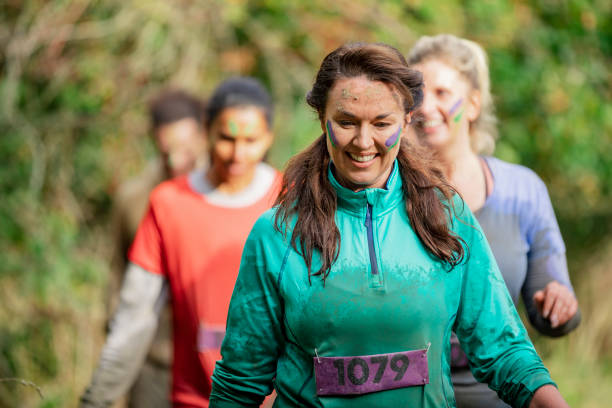 Muddy woman on charity run in country park Smiling mature woman running in Stampede event, muddy, fundraising, determination stampeding photos stock pictures, royalty-free photos & images