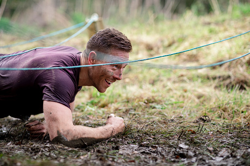 Muscular man scrambling through muddy obstacle course, determination, agility, fundraising