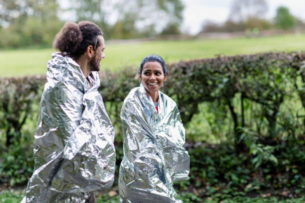Muddy couple in foil blankets walking back after outdoor event Charity runners keeping warm walking back after Stampede event, achievement, fundraising, success stampeding photos stock pictures, royalty-free photos & images
