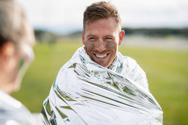 Cheerful man wrapped in foil blanket after charity event Mid adult man with foil blanket smiling after Stampede run, achievement, finish, satisfaction people covered in mud stock pictures, royalty-free photos & images