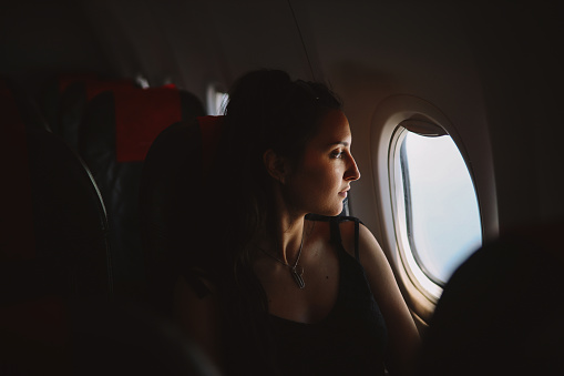 Young tourist woman sitting in the plane and looking out the window to the world below.