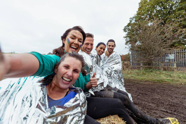 Selfie of friends with foil blankets sitting on hay bale Selfie of cheerful athletes with foil blankets after cross country charity event, achievement, fundraising stampeding photos stock pictures, royalty-free photos & images
