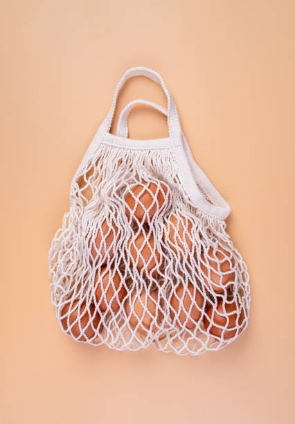 istock Eggs in a white shopping net bag isolated on beige background top view flat lay 1204009290