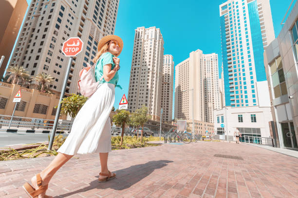 A happy Asian girl in a dress walks through a modern neighborhood with skyscrapers and office buildings. Tour and travel in Dubai A happy Asian girl in a dress walks through a modern neighborhood with skyscrapers and office buildings. Tour and travel in Dubai DUbai Apartments stock pictures, royalty-free photos & images
