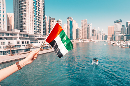 Woman holding national flag of United Arab Emirates, while standing in Marina district of Dubai