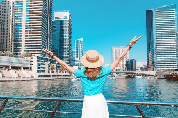 ein glückliches touristenmädchen hält die hände hoch und genießt den atemberaubenden blick auf die wolkenkratzer in der dubai marina gegend. reisen in die vereinigten arabischen emirate - united arab emirates dubai marina asia arabia stock-fotos und bilder