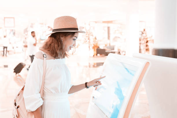 Happy asian girl using an interactive info touchscreen assistant in the shopping Mall.