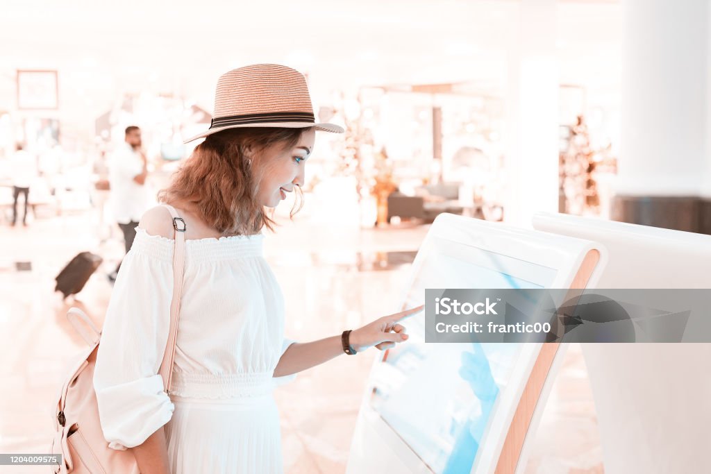 Happy asian girl using an interactive info touchscreen assistant in the shopping Mall. Touch Screen Stock Photo