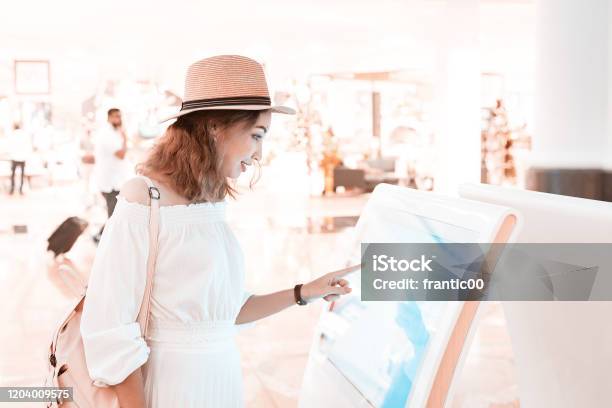 Happy Asian Girl Using An Interactive Info Touchscreen Assistant In The Shopping Mall Stock Photo - Download Image Now