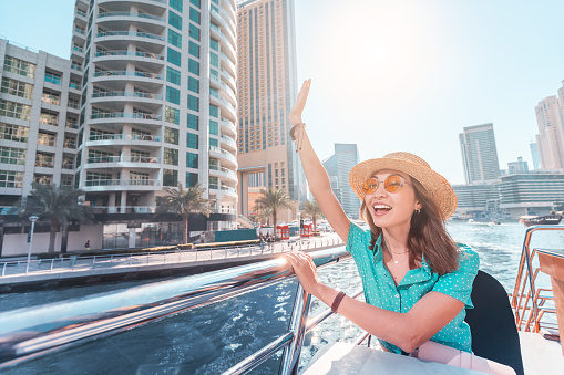 Asian girl on a boat cruise ship waving hand with skyscrapers of Marina port in Dubai