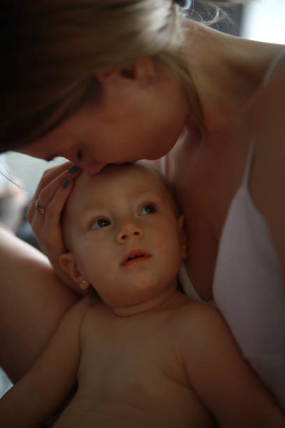A mother lovingly kisses her baby while playing together on the bed at home, highlighting parent-child bonding and love.