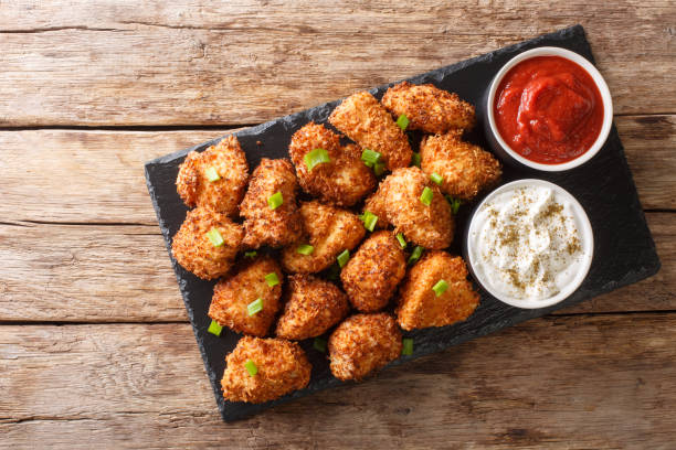 istock Portion Deep-fried chicken nuggets in coconut flakes served with ketchup and mayonnaise close-up on a slate board. Horizontal top view 1204015111