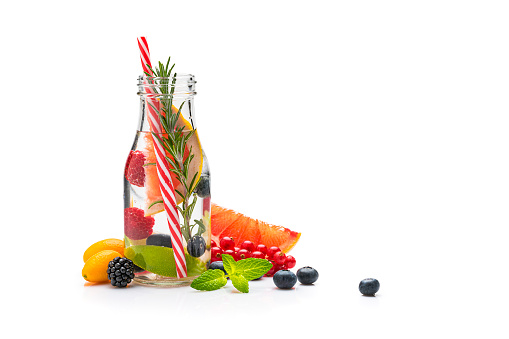 Front view of a healthy fruits infused water detox bottle isolated on white background. The composition includes lemons, mint leaves, rosemary, berries and grapefruit. The composition is at the left of an horizontal frame leaving useful copy space for text and/or logo at the right. High resolution 42Mp studio digital capture taken with Sony A7rii and Sony FE 90mm f2.8 macro G OSS lens