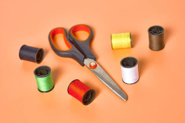 istock Scattered sewing accessories scissors and spools with colorful threads on orange tailors desk in workshop. Close-up 1204018928