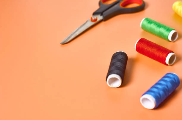istock Scattered sewing accessories scissors and spools with colorful threads on orange tailors desk in workshop. Space for text 1204018937