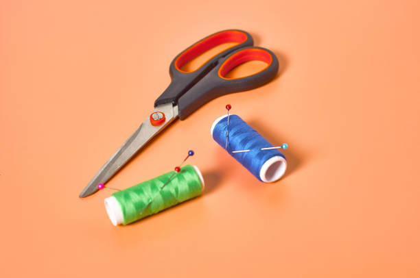 istock Sewing accessories scissors and spools with colorful threads and needles on orange tailors desk in workshop. Close-up 1204018969