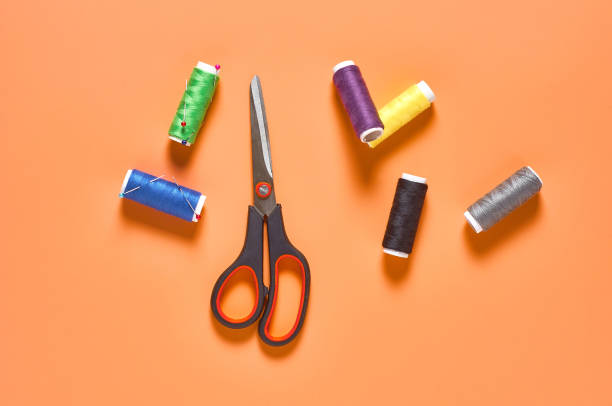 istock Sewing accessories scissors and spools with colorful threads and needles on orange tailors desk in workshop. Top view. Close-up 1204018972