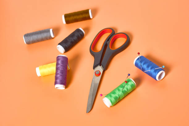 istock Sewing accessories scissors and spools with colorful threads and needles on orange tailors desk in workshop. Close-up 1204018983