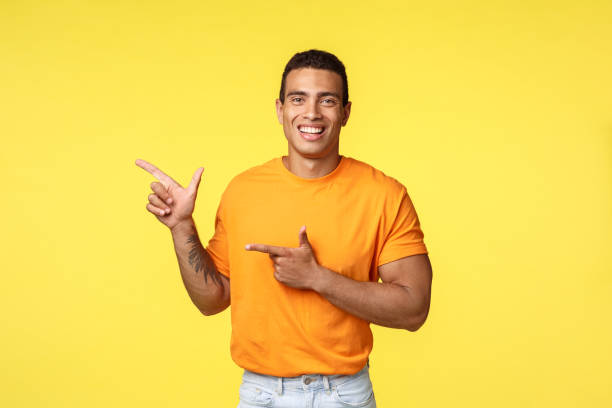 istock Cheerful modern man with tattooed arm, pointing left as promoting online store, invite guest join party, smiling joyfully, recommend try something, give advice what place visit, yellow background 1204019572