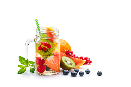 Front view of a healthy fruits infused water in a Mason jar isolated on white background. The composition includes lemons, mint leaves, rosemary, berries, kiwi fruit, orange and grapefruit. The composition is at the left of an horizontal frame leaving useful copy space for text and/or logo at the right. High resolution 42Mp studio digital capture taken with Sony A7rii and Sony FE 90mm f2.8 macro G OSS lens