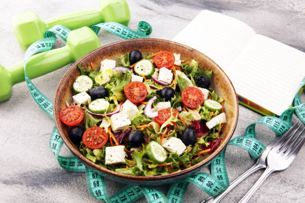 istock Authentic fresh salad in a stone cup with dumbbells excercise equipment, measuring tape on table. healthy lifestyles, good health Concept with fresh ingredients 1204026655