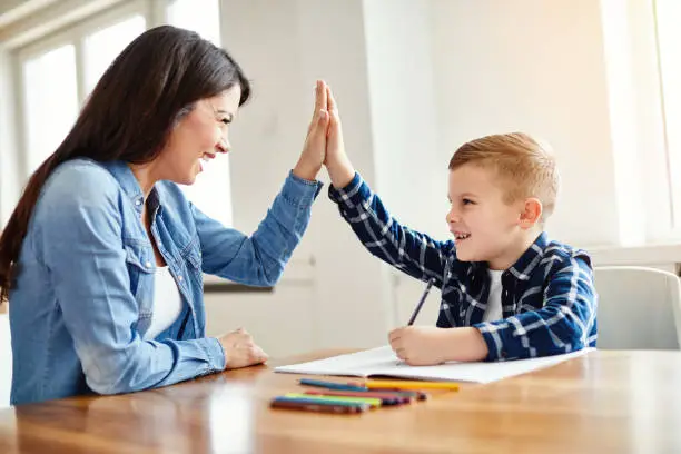 mother teaching son and helping with homework at home, son giving high five to mother