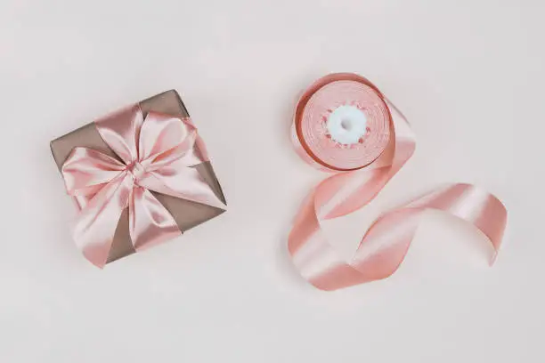 Gift box wrapped in craft paper with perfect pink ribbon on pale pink rustic background. Festive concept, top view.
