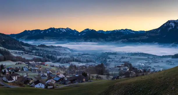 Dawn at a cold winter morning with some fog in the Bregenzerwald valley in Vorarlberg, Austria. The small village Schwarzenberg is in the foreground.