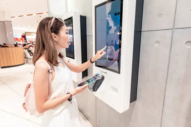 Photo of The girl makes an order in a fast food restaurant at the self-service terminal in the Mall. Modern technologies and displacement of manual labor