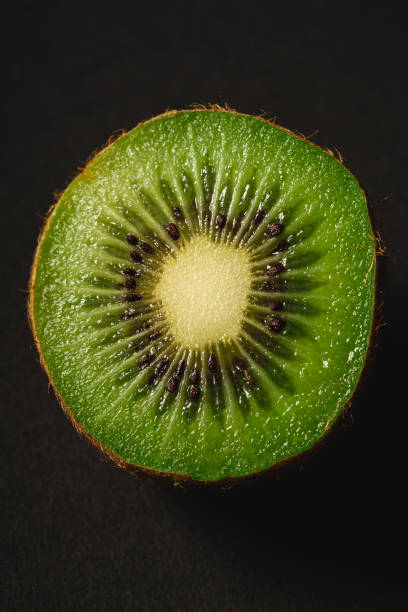 Kiwi fruit half sliced on dark black plain background, macro photography close up