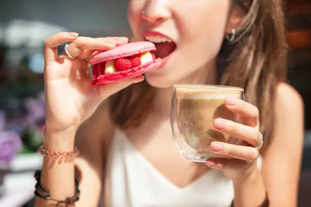 Photo of Happy asian woman tasting delicious macaroon in cafe. Breakfast and french cuisine concept