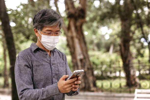 istock Mature Taiwanese man wearing pollution mask and using mobile phone 1204033865
