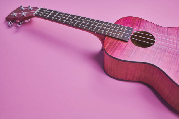 pink ukulele against pink background with copy space in matt style color photo of a pink ukulele on pink background in a matt style pink guitar stock pictures, royalty-free photos & images