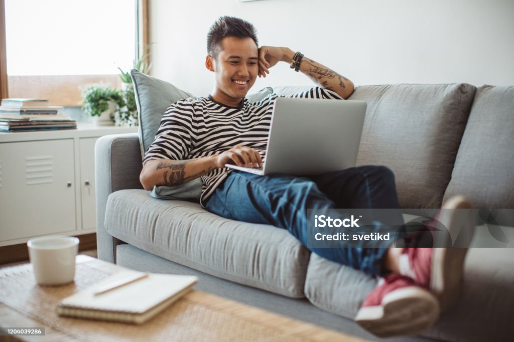 Watching new classes on laptop Young man sitting on sofa and watching something on laptop Achievement Stock Photo