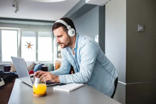 Young man is at home, with headphones and watching a online course