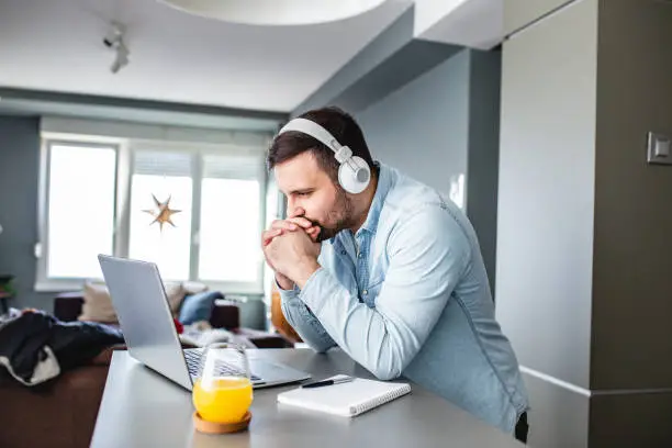 Young man is at home, with headphones and watching a online course