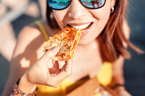 Happy girl eating Mexican fast food quesadilla on the beach. Healthy and tasty snack