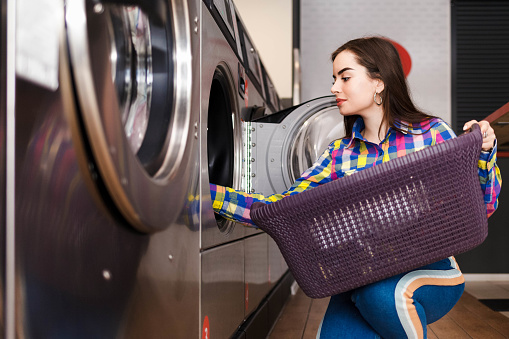 Girl loads laundry into a washing machine. woman in public laundry