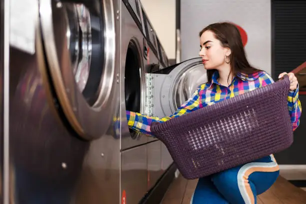 Photo of Girl loads laundry into a washing machine. woman in public laundry